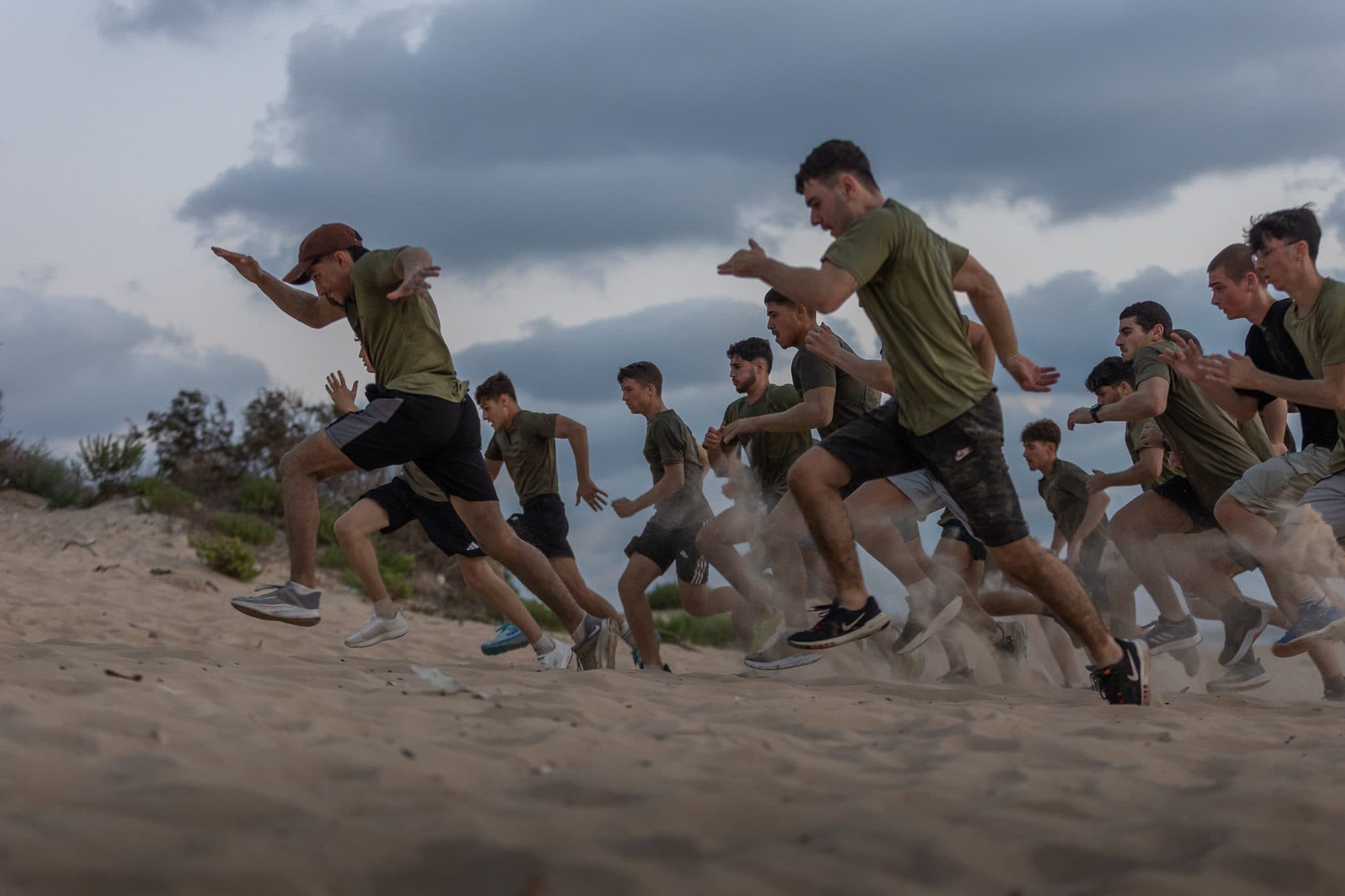 חניכי אדרנלין כושר קרבי מזנקים בריצה על דיונת חול מתחת לשמי סערה