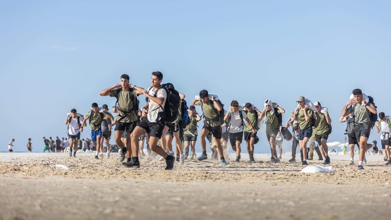 חניכי אדרנלין כושר קרבי רצים על החוף עם תיקי גב ושקי חול על הכתפיים