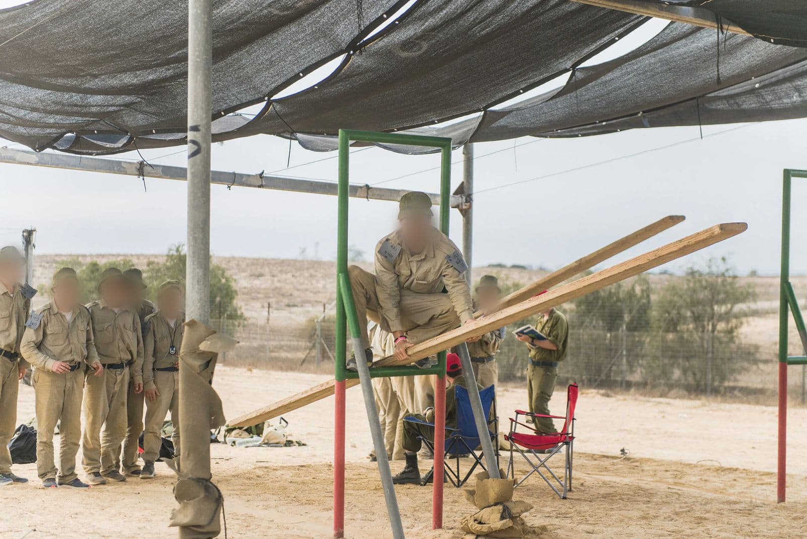 משימת צוות בגיבוש טיס: מועמד מטפס על קרשים ארוכים שנשענים על מסגרת מתכת, ומועמדים נוספים עומדים בצד ומסתכלים