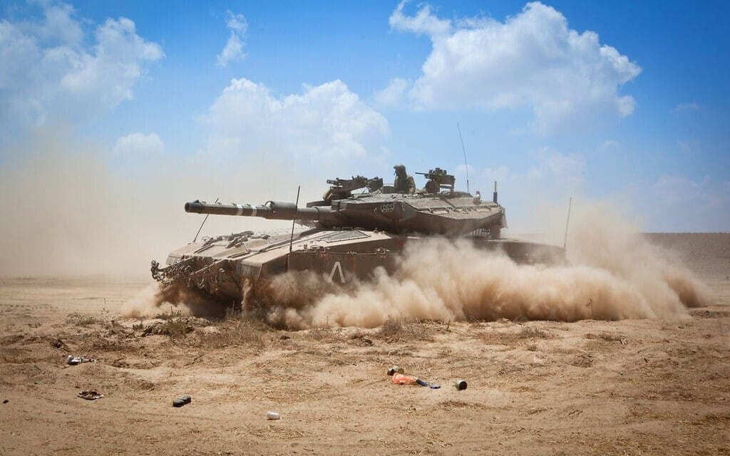 טנק מרכבה דוהר בתוך ענן אבק בשטח פתוח, ושני אנשי צוות בפתחי הצריח