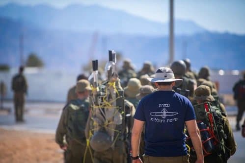מועמדים בגיבוש צוללות עם ציוד על הגב, ואיש סגל בחולצת שייטת הצוללות הולך ביניהם