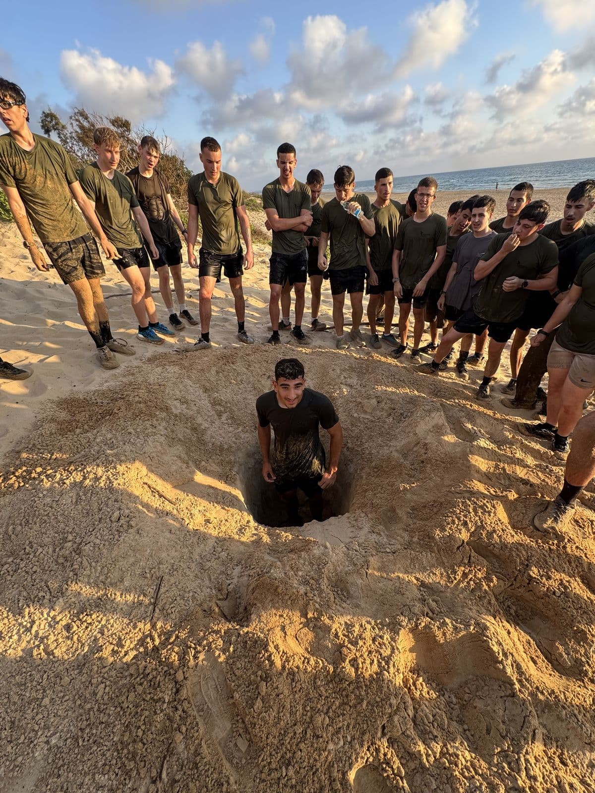חניך אדרנלין כושר קרבי עומד בתוך בור בחול, וחברי הקבוצה עומדים סביבו